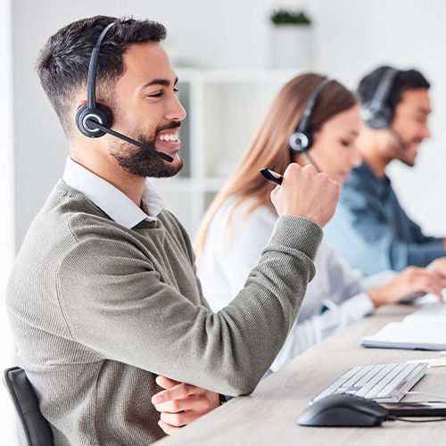 smiling male customer service representative wearing headset sitting at desk with colleagues engaged in support tasks in a modern office environment for effective communication 4 customer inquiries