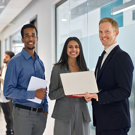 three professionals smiling in office setting with laptops collaboration teamwork and 9 essential skills
