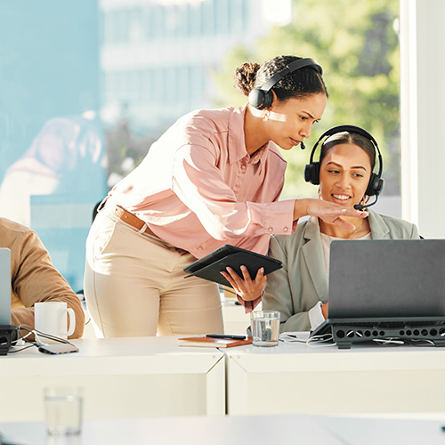 female employees in an office collaborating with headsets and tablets focused on training and communication skills for effective teamwork in the workplace
