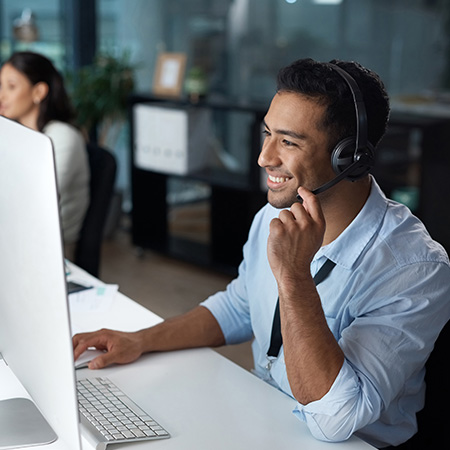 man wearing headset smiling while working on a computer in an office setting showcasing effective communication and customer service skills with seven key strategies for success