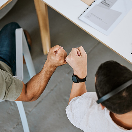 two people fist bumping in a collaborative workspace with notebooks and office tools around them celebrating teamwork and success