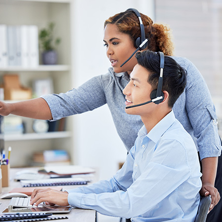 two customers in a call center working together with headsets on computers providing support and communication for four clients