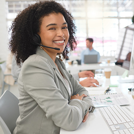 smiling woman wearing headset working at computer in office environment providing customer service with three colleagues in background