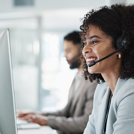 woman in headset smiling while working at computer in a call center environment with male colleague nearby providing customer support in a professional workspace focused on teamwork and communication skills for success
